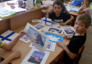 Dzieci siedzące przy stoliku z flagą Finlandii i obrazkami związanymi z Finlandią.